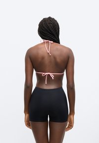 Čierne plavkové šortky s vysokým pásom kombinované s ružovým bikínovým topom na zaväzovanie za chrbtom. Látka pôsobí hladko a vytvára elegantnú siluetu.