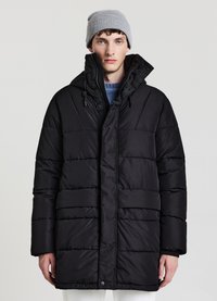 Cappotto imbottito nero con cappuccio, dotato di una chiusura con zip e dettagli con lacci. Il materiale ha una leggera lucentezza e una silhouette squadrata.