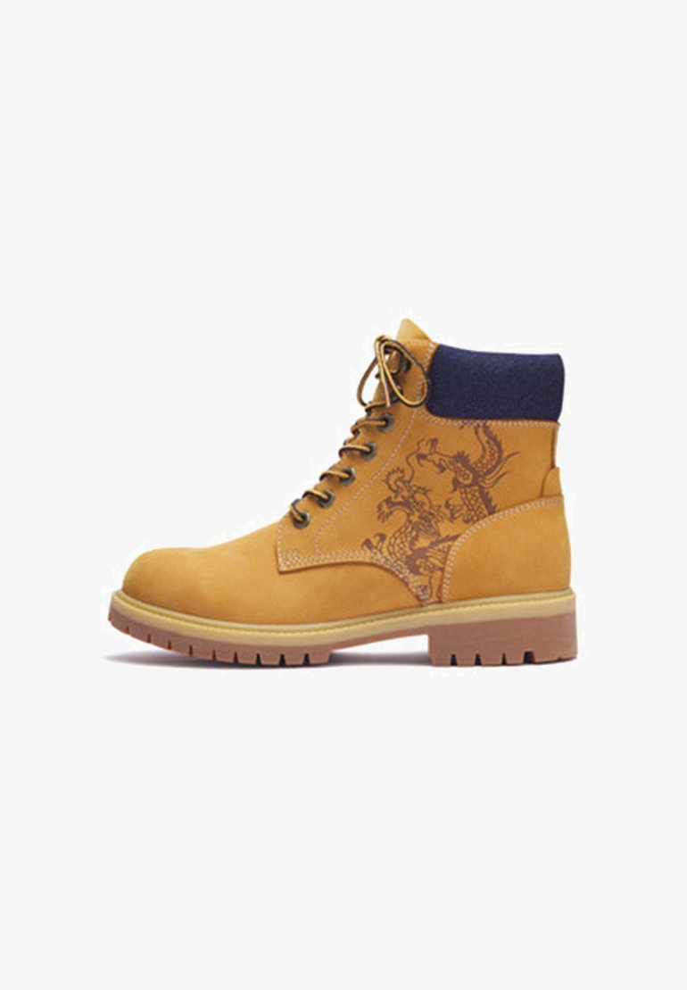 Tan lace-up work boot with black padded collar, rubber sole, and dark dragon design on side panel.