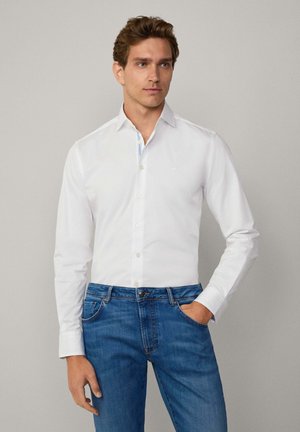 White button-up shirt with long sleeves, featuring a striped interior collar detail, paired with blue denim jeans. Smooth fabric texture.