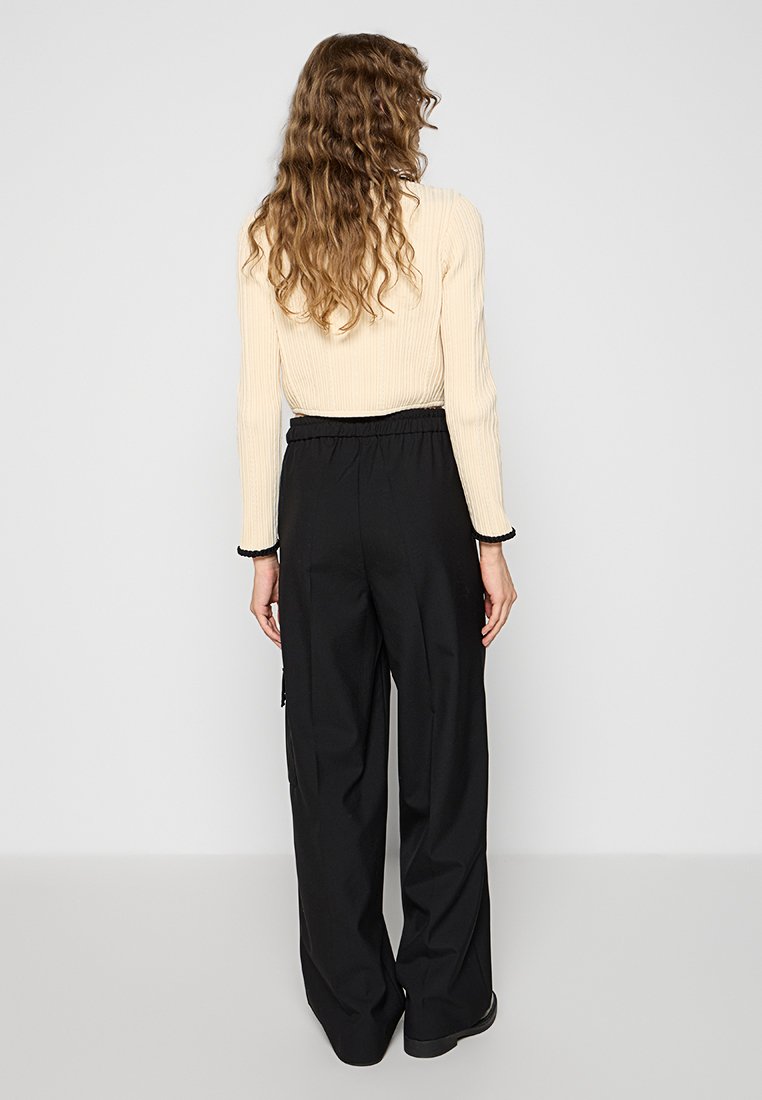 Zwarte wijde broek met een elastische tailleband, voorzien van zijzakken en een gladde stofafwerking, gecombineerd met een geribbelde beige top.