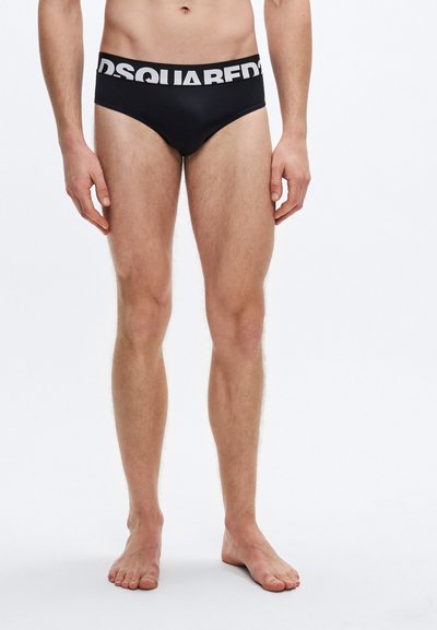 Slip noir en tissu lisse avec une large ceinture élastique portant le nom de la marque en blanc. Coupe ajustée avec une couverture minimale.