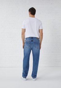Lichtblauwe denim jeans met een rechte pasvorm, vijf zakken en een klein logo-opdruk op de tailleband, gecombineerd met een wit t-shirt.