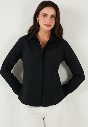 Chemise noire à manches longues avec un col pointu, fermeture par boutons, silhouette ajustée et détails de couture subtils à l'avant. Tissu au toucher lisse.