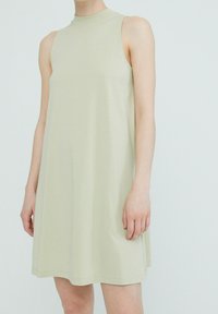 Ljusgrön ärmlös klänning med hög halsringning, tillverkad av mjukt tyg. Har en löst sittande passform med minimalt design och inga synliga mönster.