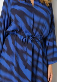 Modré a námořnické šaty s vzorem, mají výstřih do V, dlouhé rukávy a nastavitelný stahovací pas, vyrobené z hladkého materiálu.