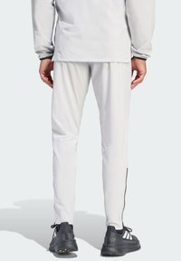 Białe spodnie sportowe o zwężanym kroju z bocznymi zamkami błyskawicznymi, w zestawieniu z czarnymi trampkami z białymi paskami. Gładka faktura.