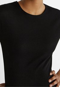 Top nero a costine con scollatura rotonda e maniche corte, realizzato in un tessuto texturizzato per una silhouette aderente.