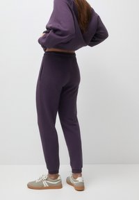 Fioletowy krótki sweatshirt z długimi rękawami oraz dopasowane joggery z elastycznym paskiem w talii i bocznymi kieszeniami, sparowane z szarymi sneakery.