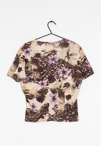Beige shirt met korte mouwen met een bruin en paars bloemen- en vlinderprint, hangend aan een zwarte hanger tegen een witte achtergrond.