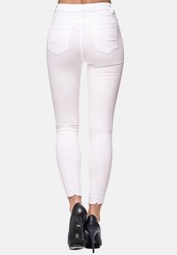 Jeans ajustados blancos de cintura alta, con bolsillos traseros y detalles desgastados en el dobladillo. Combinados con tacones altos negros.