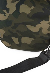 Bolsa con estampado de camuflaje fabricada en un tejido texturizado y tejido en tonos de verde y marrón. Cuenta con una correa negra ajustable y detalles de hebilla.