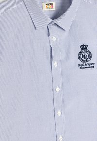 Camisa de botones a rayas azul y blanca con cuello, que presenta un logotipo bordado en el lado izquierdo del pecho y botones blancos. Material de algodón.
