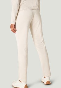 Cream-colored, stretchy, tapered pants with a soft texture, paired with white sneakers featuring a tan rubber sole.
