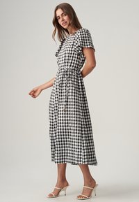 Black and white gingham dress with short ruffled sleeves, tying waist, and a flowing skirt. Worn with open-heeled sandals.