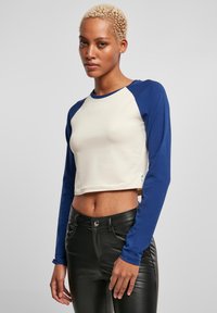 Korte longsleeve shirt in crème en marineblauw, met een ronde halslijn en een aansluitend ontwerp. Gecombineerd met high-waisted zwarte broeken.