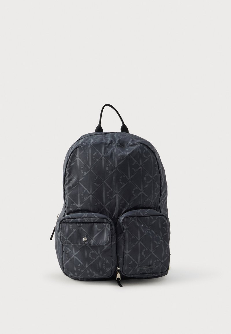 Mochila de nailon en gris oscuro con un patrón geométrico. Cuenta con correas acolchadas para los hombros, asa superior y dos bolsillos frontales con cremallera.