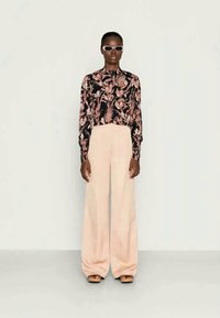 Blusa de manga longa com estampa floral em preto e rosa, combinada com calças largas de um rosa pálido. Modelo usando óculos de sol elegantes e sapatos castanhos.