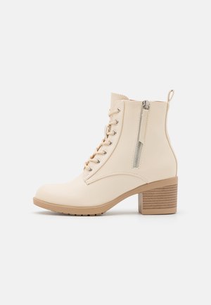 Bottine beige en cuir synthétique lisse avec un laçage à l'avant, une fermeture éclair sur le côté et un talon carré avec des rainures horizontales.
