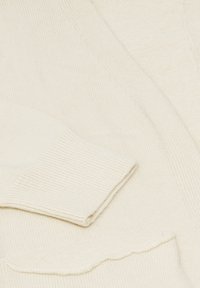 Krämfärgad stickad tröja med ribbade mudd och en vågig kant på fickan. Mjuk textur med en avslappnad och ledig design.