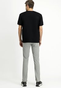 Maglietta nera a maniche corte con scollo rotondo, abbinata a pantaloni slim-fit grigi chiari e scarpe da ginnastica nere. Tessuto morbido, design minimale.