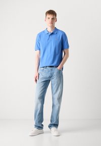 Helles blaues Polohemd mit Kragen, kombiniert mit hellblauen Jeans. Das Outfit umfasst weiße Sneakers und sorgt für einen lässigen Look.