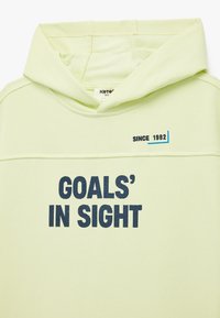 Jasnozielona hoodie z miękkiego materiału z kieszenią kangurzą. Posiada wyszyty tekst "CELE W ZASIĘGU RĘKI" oraz "OD 1982 R." w granatowym kolorze.