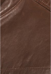 Hnědá kožená látka s hladkým povrchem, s jemnými záhyby a švem podél jednoho okraje. Minimální detaily, jednotná barva.