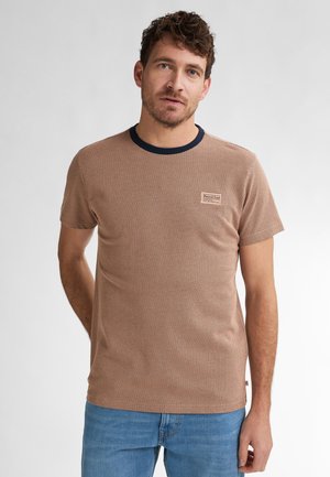 Brown textured t-shirt with a navy blue collar. Features a small logo patch on the chest and short sleeves. Worn with blue jeans.