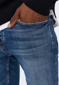 Vaqueros de mezclilla azul con un diseño clásico de pierna recta, que cuentan con un bolsillo con costura visible y un acabado de tela texturizada.