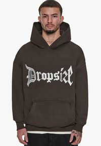 Barna kapucnis pulóver, elülső kenguru zsebbel és nagy, fehér gótikus felirattal "DropsiZ" a mellkason. Puha anyag, laza szabás.