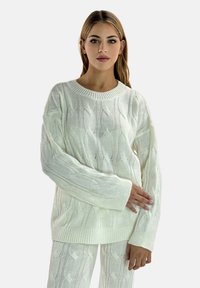 Hvid kabelstrik sweater med bred rund hals og lange ærmer, prydet med teksturerede mønstre og ribbede manchetter.