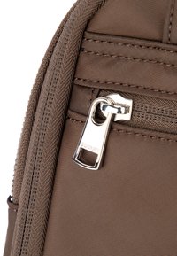 Róg brązowej nylonowej torby z srebrnym zamkiem błyskawicznym i wytłoczonym logo. Charakteryzuje się fakturowaną tkaniną i przeszyciami wzdłuż krawędzi.