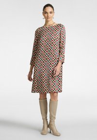 Bedrucktes Shiftkleid mit mehrfarbigen geometrischen Mustern, runder Ausschnitt und langen Ärmeln, kombiniert mit knielangen beigefarbenen Stiefeln.