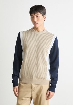 Suéter de punto acanalado beige con mangas azul marino y paneles laterales blancos. Presenta un cuello redondo y un acabado texturizado.