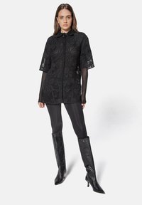 Black lace shirt dress with short sleeves and a collar, featuring floral patterns. Paired with black leggings and knee-high textured boots.