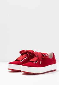 Zapatillas de plataforma de ante rojo con suela texturizada blanca, cordones gruesos rojos y ojales plateados, con punta redondeada y un interior suave.