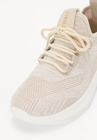 Baskets tricotées beiges avec un motif texturé, bout rond, lacets crème et semelle rembourrée. Présente un logo subtil au niveau du talon.