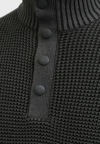 Suéter tejido de color gris oscuro con un cuello de canalé, que presenta cuatro botones redondos y texturizados y un patrón parecido a un gofre en el cuerpo.