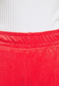 Röda manchesterbyxor med en ribbad vit topp, som har en avslappnad passform och elastisk midja. Tyget har en mjuk, texturerad yta.