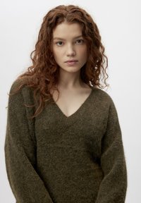 Pulover verde cu decolteu în V, realizat dintr-un material tricotat moale și texturat, având mâneci lungi și largi și o croială confortabilă.