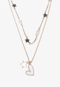 Collier superposé en ton or avec des accents en forme d'étoile noire, des perles de culture blanches et un pendentif en forme de cœur avec un design transparent.
