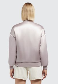 Jachetă bomber de culoare mauve deschis, cu un finisaj satin smooth, manșete și tiv ribbed. Prezintă o croială lejeră și un design minimalist.