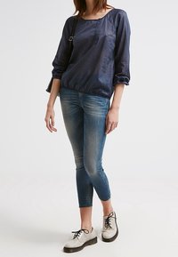 Námořnická blůza s puntíky a nařaseným lemem, spárovaná s světle modrými skinny džíny a šněrovacími dvoubarevnými botami s texturovaným povrchem.