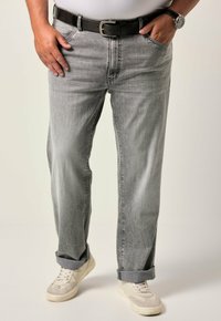 Jeans in denim grigio chiaro con sbiaditure visibili, vestibilità dritta, risvolti alle caviglie, abbinati a sneakers bianche e una cintura nera.