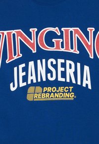 Blå bomull T-skjorte med fet rød og hvit tekst: "WINGING JEANSERIA" og "PROJECT REBRANDING" i gult, grafisk design.
