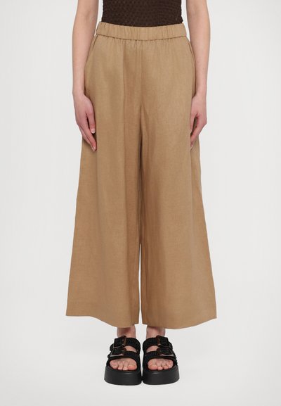 Pantalons larges en lin beige avec une taille élastique, associés à des sandales à plateforme noires avec de grandes boucles et des sangles texturées.
