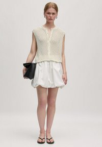 Ärmelloses Stricktop aus Baumwollmischung mit Netzmuster, kombiniert mit einem weißen, puffigen Minirock. Eine schwarze Clutch und Flip-Flops runden den Look ab.
