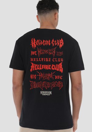 Schwarzes T-Shirt mit mehreren roten grafischen Texten, darunter "Hellfire Club" und "Stranger Things", in verschiedenen stilisierten Schriftarten und Größen.