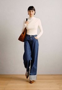 Long-sleeve cream top paired with high-waisted blue denim wide-leg trousers, featuring a cuffed hem and brown leather shoulder bag.